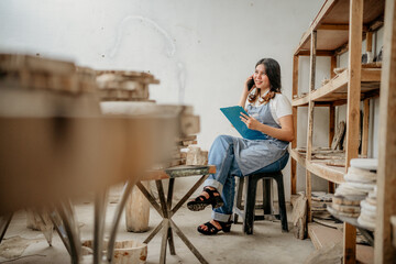 candid shot of a stone craft businesswoman making a phone call while holding a clipboard in a warehouse