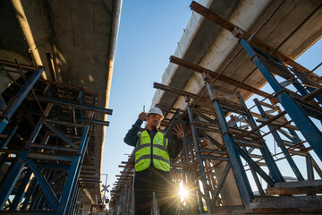 Mature engineer architect in safety and helmet costume working on a tablet on a tollway...