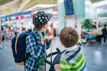 european siblings boys with backpack checking flight time at departure board in airport