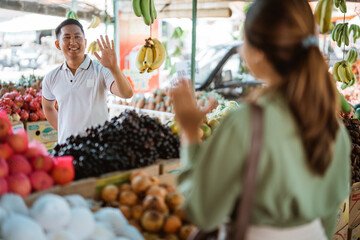 asian man smiling and waving his hand to his friend while meeting her at fruit shop