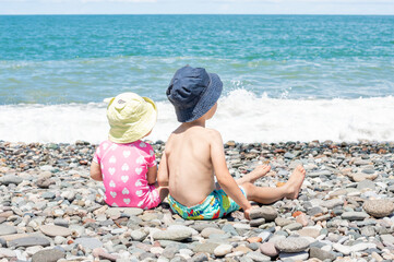 Two children sitting on the stone on the seacoast in summer. Concept of the family vacation and tourism.