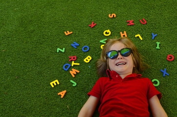 A preschooler plays with English letters. Learning the alphabet in kindergarten. The boy laughs - a fun lesson on the grass Copy Space