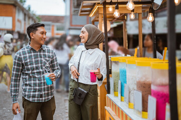 portrait of happy young muslim couple buy drink from a street vendor - obrazy, fototapety, plakaty