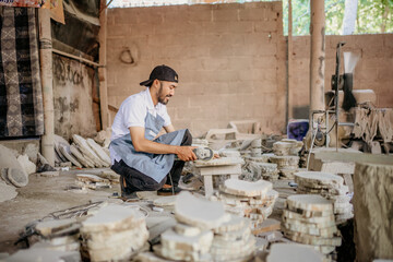 side view of a stone craft worker squatting while cutting stones using a grinder in the workshop