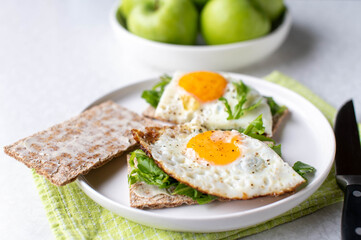 Gluten free and vegetarian breakfast plate with low carb cripbread, arugula, fried eggs and green apples on white background