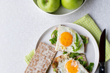 Healthy breakfast with fried eggs, arugula, crispbread and green apple on a light background