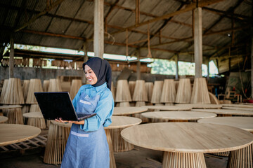 Veiled woman using laptop computer while standing in wood craft shop