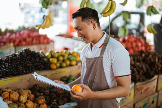 male seller in apron holding the mandarin fruit and checking the fruit list at the clipboard