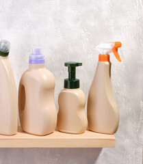 Detergents and cleaning supplies in beige different bottles on a wooden shelf.