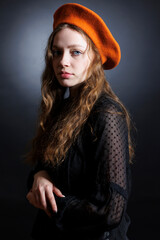 Portrait of a sad young woman in an orange beret and long curly hair on a dark background. - 622579551