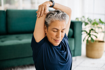 Overhead tricep stretch during yoga: Senior woman doing an arm exercise at home