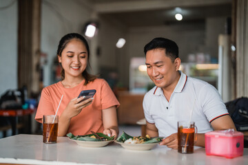 Asian couple photographing their food for social media while eating lotek at traditional food stalls