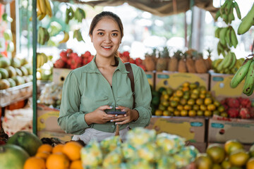 female customer smiling while standing and holding the phone at the fruit shop