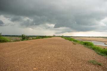 stretched pebbled way touching the horizon along the mayurakshi river uder the cloudy monsoon sky