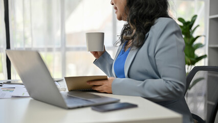 A senior businesswoman sipping coffee while working on her business work at her desk.