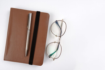 An e-book in a brown case or a notebook with round stylish optical glasses, a pen on a white...