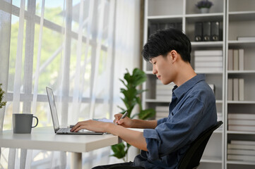 A focused young Asian male office worker is working on his work on his laptop