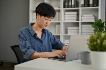 A smart Asian male office worker is working on his work on his laptop at his desk