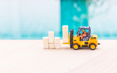 Miniature worker in safety suite on forklift truck and wooden cubes, cargo industry concept