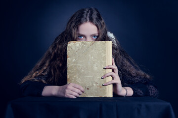 Portrait of a frightened young woman with a book on a dark background. - 622585320