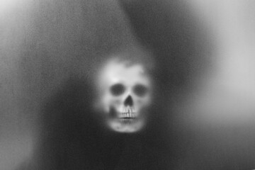 Mysterious man holding a skull in his hand standing behind frosted glass looking mysterious and...