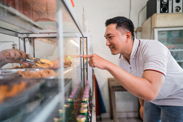 male customer choosing food by pointing finger from outside the glass display window of a food stall