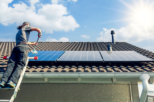 man holding mop cleaning solar panels. cleaning of solar modules with water. close-up of solar panels on the roof on sunny sky. Mop cleaning. Washing Solar modules in summer season on sunny day. 