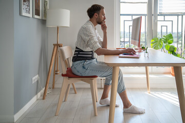 Focused male freelancer wearing lumbar brace sitting at table using computer, young man use...