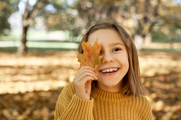 Caucasian girl covering an eye with autumn leaf