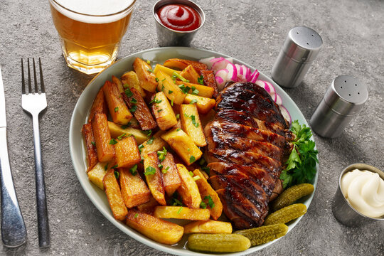 American lunch with juicy steak and beer, served with french fries, radishes and herbs