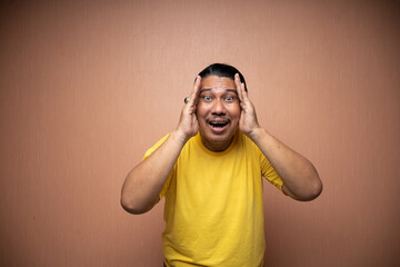 old asian man wearing yellow tshirt playing peek a boo with excited expression in plain background...