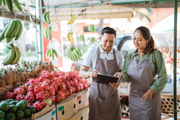 beautiful fruit seller pointing on the clipboard that holding by the male seller while checking the...