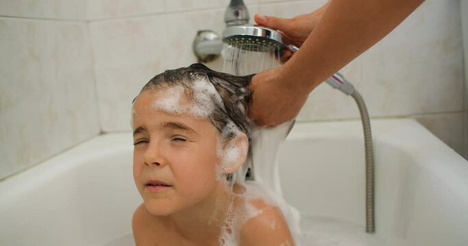 A mother washes her daughter's hair in the bathroom. Happy parents help their children and have fun together. High quality 4k footage