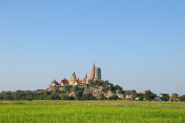 Obraz premium Wat Tham suea or Tiger cave temple on hill surrouned rice paddy and light blue sky in Kanchanaburi province, Thailand.