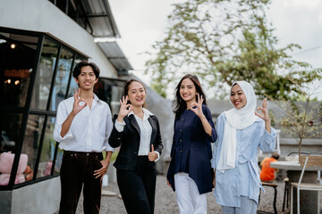 Group of cheerful young businesspeople wearing casual clothes with okay hand gestures standing in a coworking space