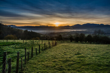 A serene meadow in Asturias at dawn, enclosed by a fence, with a breathtaking mountainous valley as the backdrop.