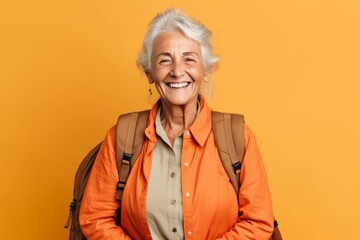 Portrait of a smiling senior woman with backpack isolated over yellow background