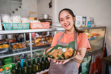 Attractive Asian girl shows a plate of pecel food at a food stall