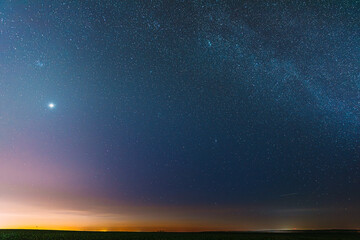 Night Starry Sky With Glowing Stars Above Countryside Field Landscape In Early Spring. Bright Glow...