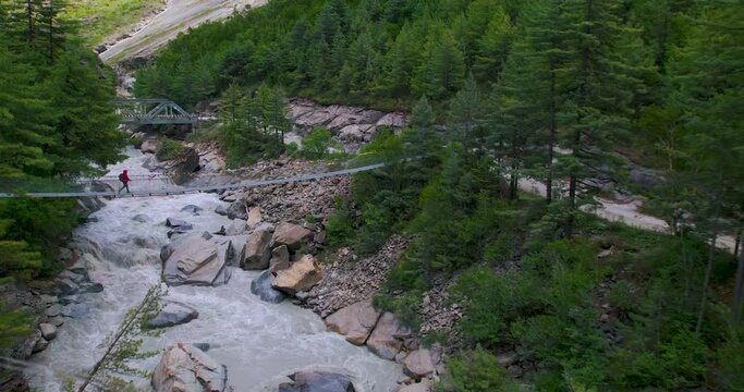 Drone shot of a man crossing suspension bridge at Manang Nepal enjoying the greenery and river flowing downwards. Adventurous and exciting trek with absolutely amazing nature peace and calm. 4K