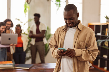 closeup african man looking at his mobile phone while in the background his classmates out of focus...