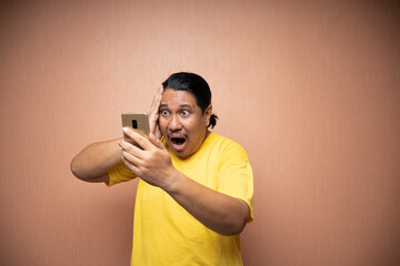 old asian man wearing yellow tshirt holding handphone and using it to texting or video call with...