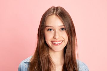 Fototapeta premium Portrait of young beautiful woman, student looking at camera and smiling against pink studio background. Happy. Concept of human emotions, fashion, youth, lifestyle, female beauty, ad
