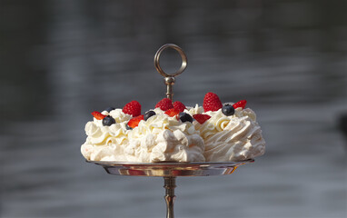 Pavlova desserts embellished with summer berries fruits, raspberries, strawberries and blueberries, closeup with no people around. - obrazy, fototapety, plakaty