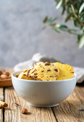 Florence cookies or fiorentine biscuits with almonds in white bowl, almonds on plate, olive tree branch, napkin over wooden table with grey background