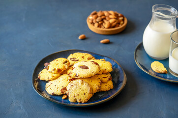 Florence cookies or fiorentine biscuits with almonds on blue ceramic plate, glass of milk and milk jug, almonds on plate over dark blue background