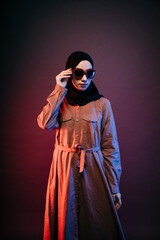 muslim woman wearing black hijab orange long dress posing for the camera by holding sunglasses and looking sideways