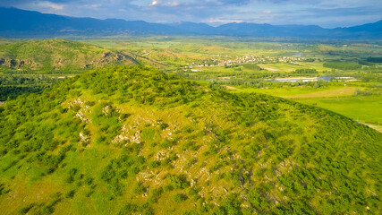 Panoramic drone view of the mountains and the valley with the village at the foot of the mountains in early spring, in front of the approaching thunderclouds. Rupite area (Church of Vanga), Bulgaria