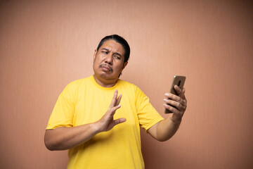 old asian man wearing yellow tshirt holding handphone and using it to texting or video call with each other in plain background isolated