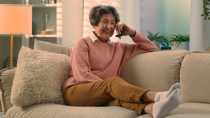 Obraz premium Relaxed happy laughing old woman on cozy sofa talking on smartphone laugh discuss funny news carefree smiling senior grandmother at comfy couch at home elderly lady female retired speak mobile phone